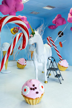 In a vibrant and surreal candy-themed space, a majestic white unicorn stands amidst giant cupcakes, lollipops, and pink fluffy clouds, inviting all to enter a world of sweet imagination and joy.の写真素材