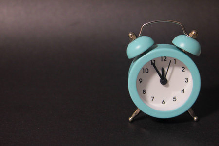 A small blue alarm clock on the dial of which is 23:55, which stands on a black background....