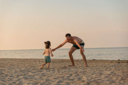Happy father catch little daughter on beach holding opened arms.の写真素材