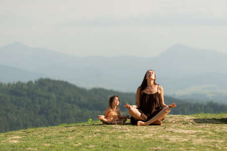 Mother in pose of lotus in mountains with little daughter.の写真素材