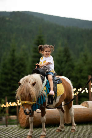 Pretty emotion baby girl riding a pony and smiling.の写真素材