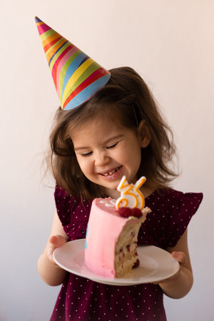 Portrait of pretty birthday girl toddler holding cake with candle.