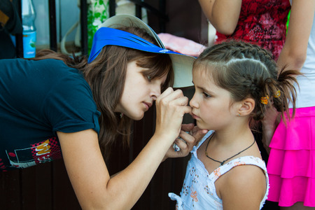 VOLGOGRAD, RUSSIA - JUNE 26, 2010: Artist paints mask on a girl's face on a children's holiday in the park in Volgogradのeditorial素材