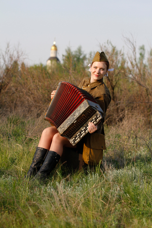 Pretty Soviet female soldier in uniform of World War II sits with an accordion on a suitcaseの写真素材