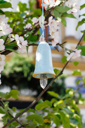 Blue ceramic bell with a tongue in the form of a feather hanging on a branch of flowering tree