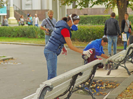 Moscow, Russia - August 29, 2015: Street female artist in a respirator using can with spray paint draws on a wooden bench at VDNH in Moscowのeditorial素材