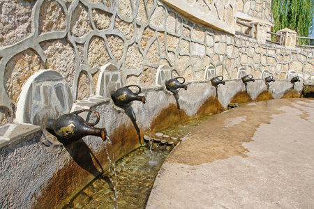Spring water flows from metal jugs hanging on the font building on "Kudykina mountain" in Lipetsk oblastの写真素材
