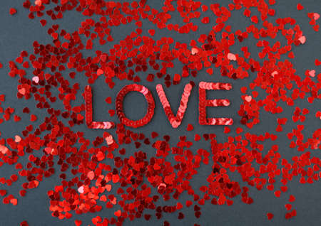 Inscription of "Love" embroidered with red sequins on black textured background with scattered random sequins in form of heartsの写真素材