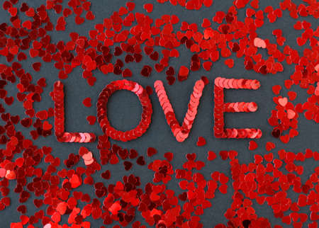 Inscription of "Love" embroidered with red sequins on black textured background with scattered random sequins in form of heartsの写真素材