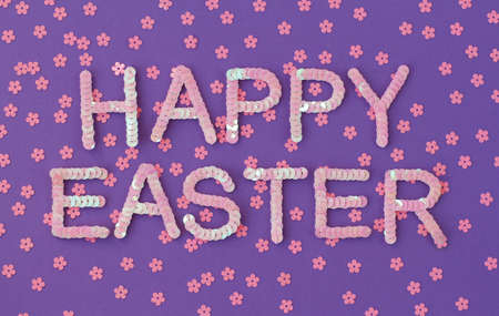 Inscription of "Happy Easter" embroidered with pink sequins on purple textured background with scattered random sequins in form of flowersの写真素材