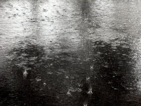 Raindrop hitting on asphalt road. Background flooded road with splash from the raindrops. Rain on pavement creating ripples.の写真素材