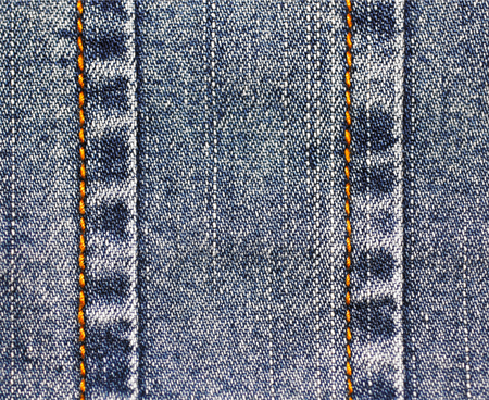 Background of denim fabric with seams. Blue jeans cloth stitching with orange thread. Old vintage backdrop with place for your text. Grunge texture in retro style. Horizontal orientation.の写真素材
