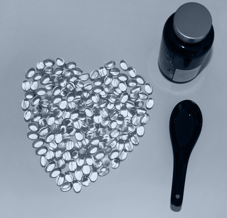 Gel pills of Omega-3 lying in the shape of a heart on white background. Vitamin E capsules, a black spoon and pharmaceutical bottle. Advertising healthy lifestyle, of careful attitude to the health.の写真素材