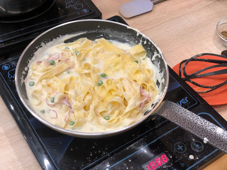 Fettuccine carbonara with ham and green peas in a panの写真素材