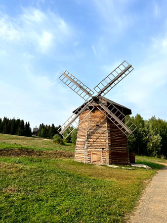 Old wooden windmill on a green meadow against the blue sky