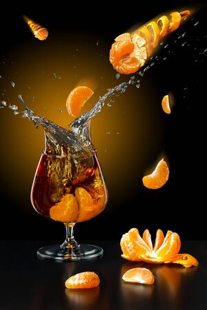 Cognac in a glass and tangerines falling into itの写真素材