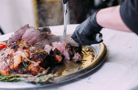 Hot meat on a metal plate cuts the cook with two knivesの写真素材