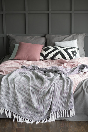 a bed in an interior with pillows and plaids near a wall with geometryの写真素材