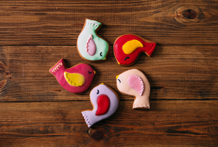 
gingerbread birds of different colors lie in a circle in the center on a wooden backgroundの写真素材
