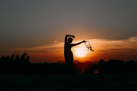 girl at sunset with an ornament in ethno-style Indian necklace beads with feathers silhouetteの写真素材