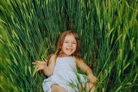 little girl in a white dress on a field of wheat green fell and laughsの写真素材