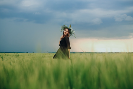 young beautiful girl with a wreath of flowers walking through the spring fieldの写真素材