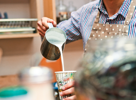 barman pours milk with foam into a glass of coffeeの写真素材
