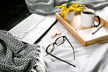 mockup spring set on the bed with a gray plaid laptop flowers mimosa flash drive glasses cup of coffeeの写真素材