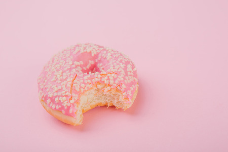donut with pink icing  bitten on one side on a pink backgroundの写真素材