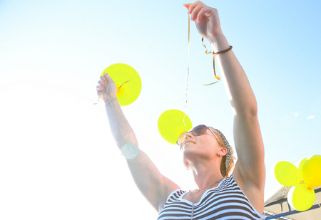 girl in a striped dress outside launches balloons yellow against the sky and sunの写真素材