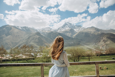 girl in a dress one near a house in the hills looking at the mountains with snow peaksの写真素材