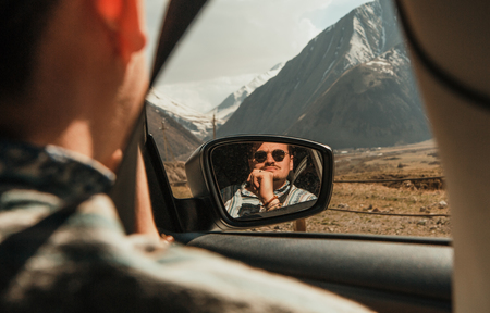 man in sunglasses looking at the mountains with car window reflected in the mirrorの写真素材