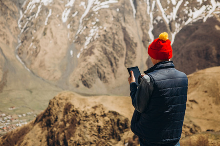 girl with a smartphone is standing on a mountain with a beautiful landscape of a mountain range with snowの写真素材