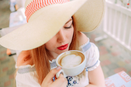 girl in a cap drinking cappuccino in a cafe at a table outside on the terraceの写真素材