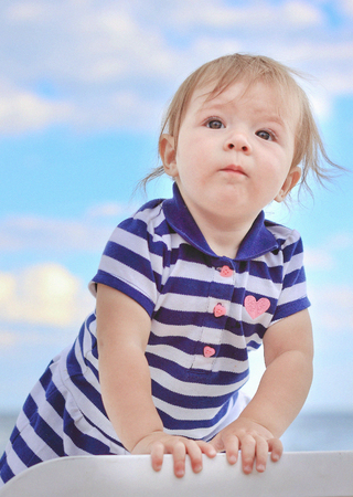 little girl on a chaise longue in a striped dress against the skyの写真素材