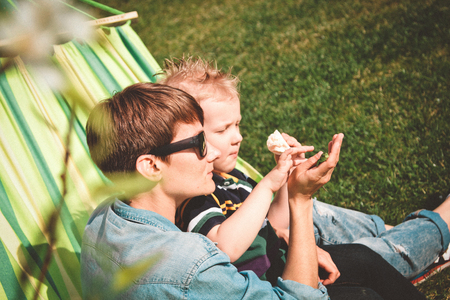 Mom and son are sitting in a hammock and stroking a green lizardの写真素材