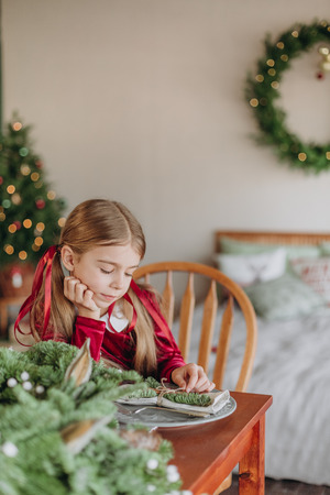 girl in a burgundy dress decorates a Christmas tree in a rustic roomの写真素材