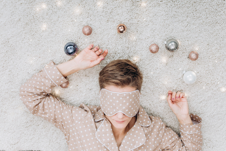 girl in beige pajamas and a sleep mask 
lies sleep with Christmas decorations balls golden grayの写真素材