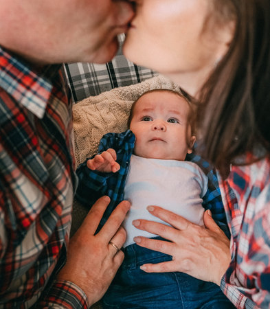 baby carefully looks at parents kissing home style in shirts