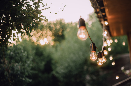 retro garland lamps outside shine in the evening on the walls of the houseの写真素材
