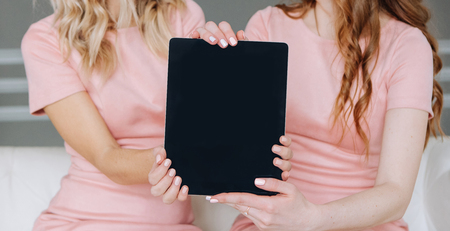two girls in a pink dress together show a picture of a tablet in front of the centerの写真素材