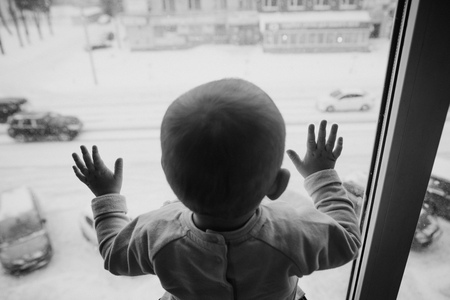 child looks out the window to the street, outside it began to snowの写真素材