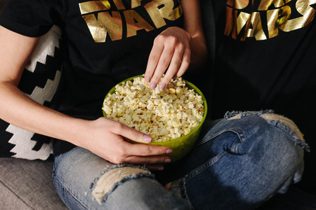 girl is sitting on the couch and eating popcorn with a deep bowlの写真素材