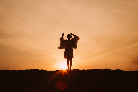 woman on top of the mountain rejoices and dances at sunsetの写真素材