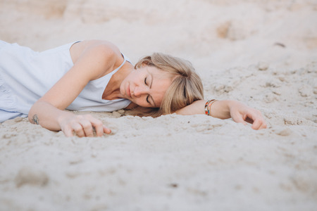 girl in a sundress lies on the sand sad crying longing loneliness conceptualの写真素材