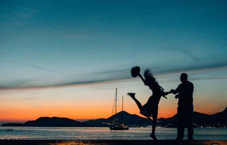 silhouettes of a loving couple on the seashore with a yacht at sunsetの写真素材