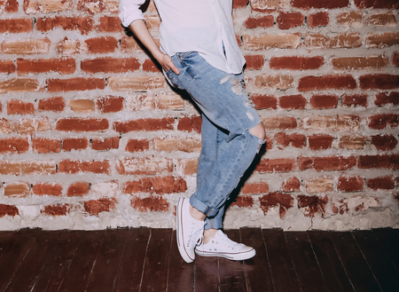 woman posing indoors studio in jeans and sneakers on brick wall backgroundの写真素材