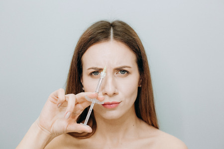 Injection cosmetology woman with beautiful skin and lips holds a syringe with a preparation for rejuvenationの写真素材