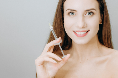 Injection cosmetology woman with beautiful skin and lips holds a syringe with a preparation for rejuvenationの写真素材