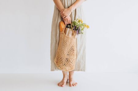 woman in a linen dress with groceries and wild flowers in a string bag in a mesh bag packageの写真素材